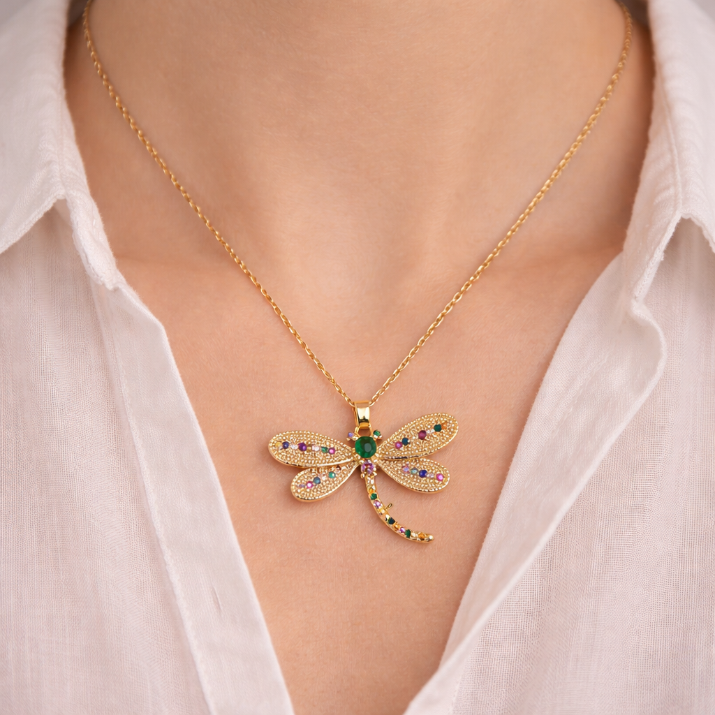Gold necklace with a dragonfly pendant worn by a person in a white shirt.