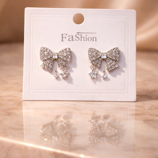 Bow-shaped earrings on a 'Fa$ion' branded card against a beige background