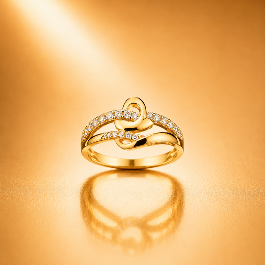 A gold ring with a heart-shaped design and small clear stones, displayed on a warm gold reflective surface.