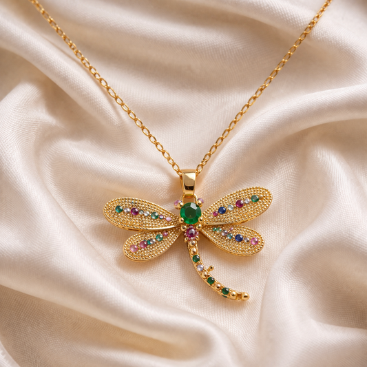 Gold dragonfly pendant necklace with gemstones on a beige satin background