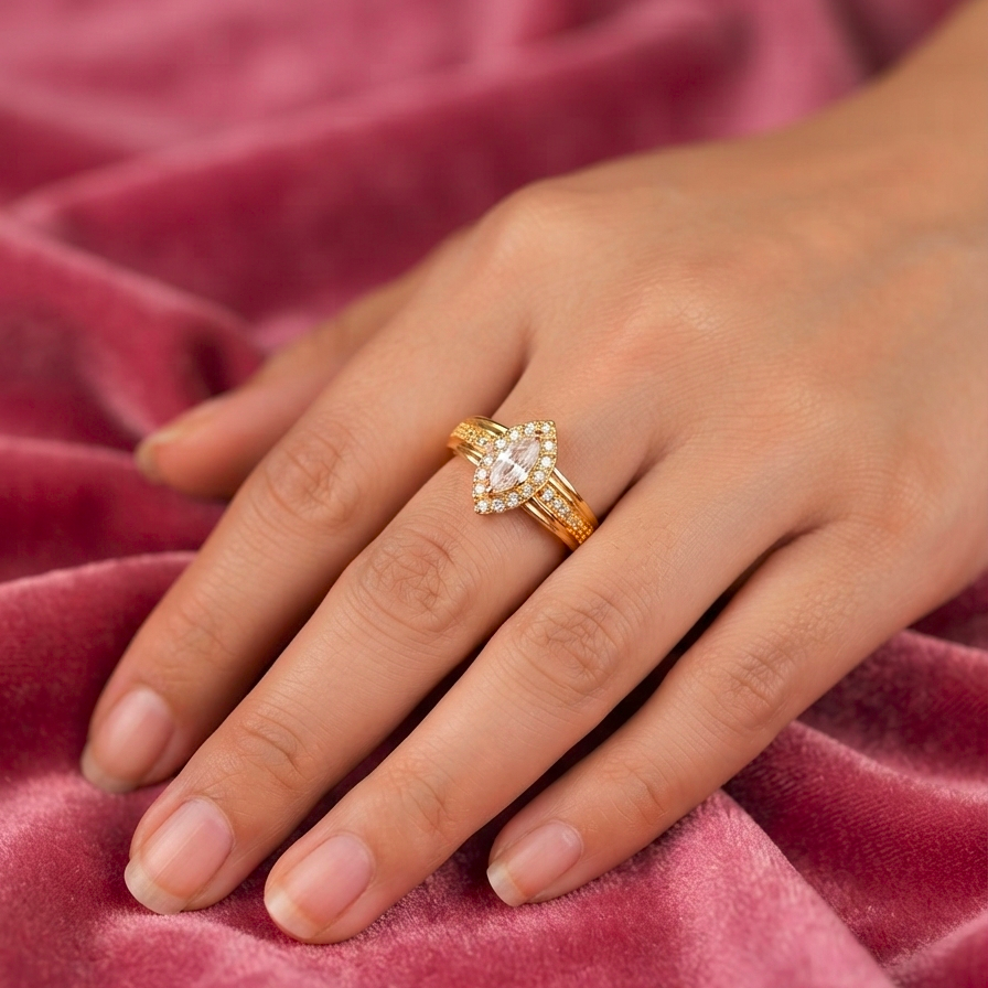 A gold ring with a marquise-cut center stone and small side stones, worn on a hand resting on a textured pink velvet surface.