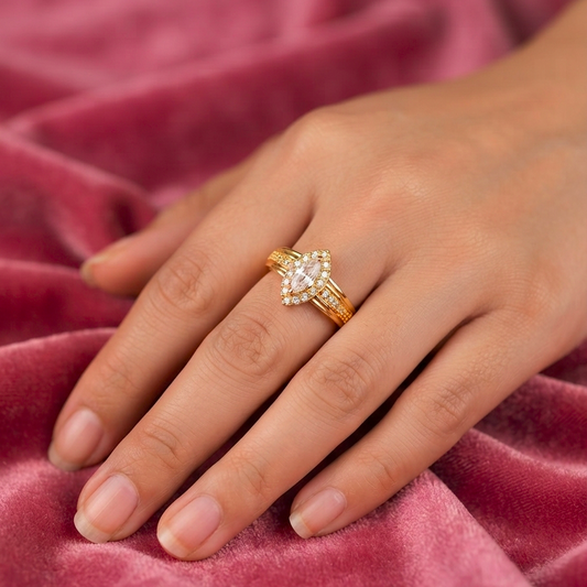 A gold ring with a marquise-cut center stone and small side stones, worn on a hand resting on a textured pink velvet surface.