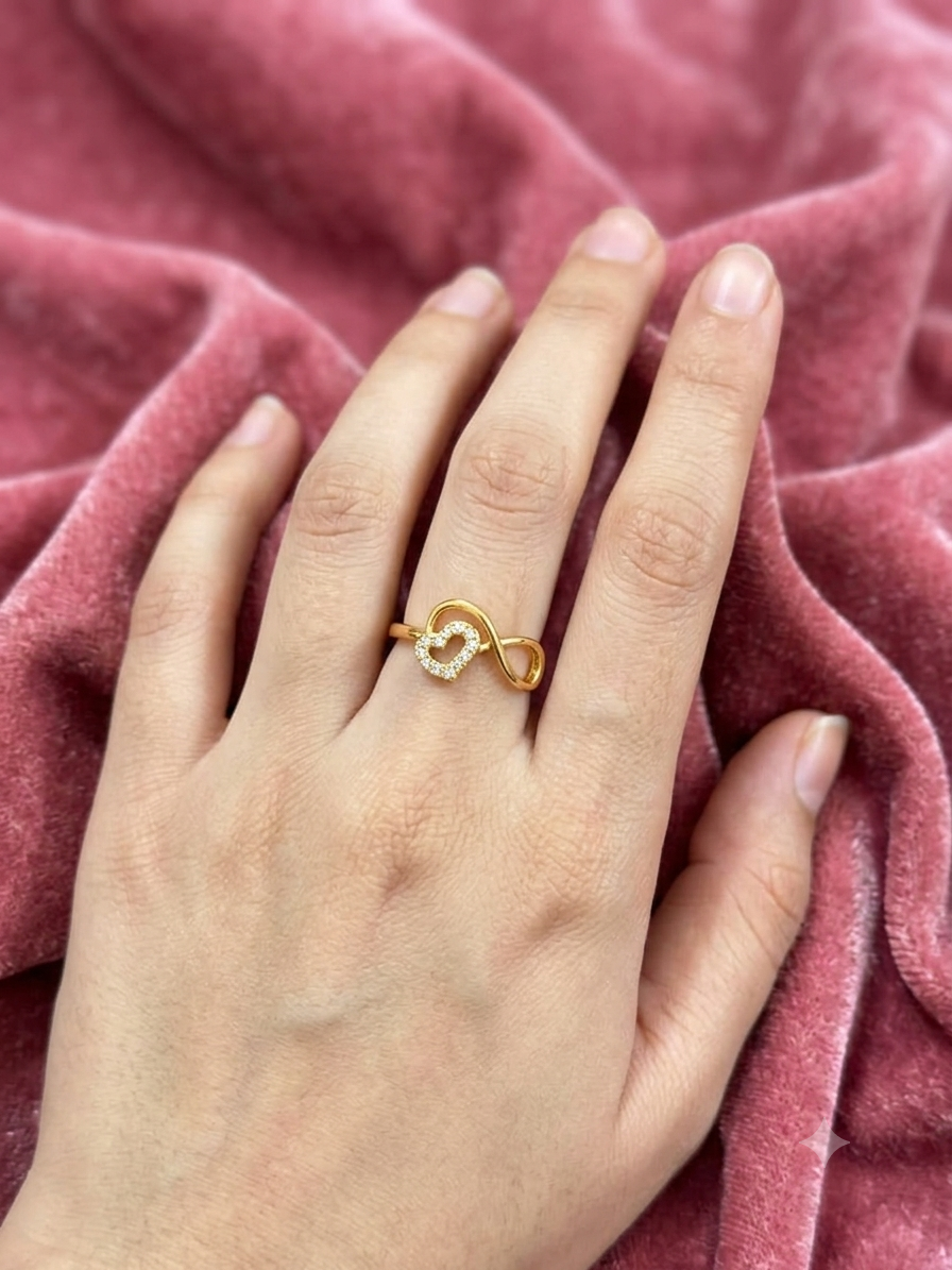 A gold infinity ring with small clear stones on the ring finger of a hand, resting on a textured dusty pink velvet fabric.