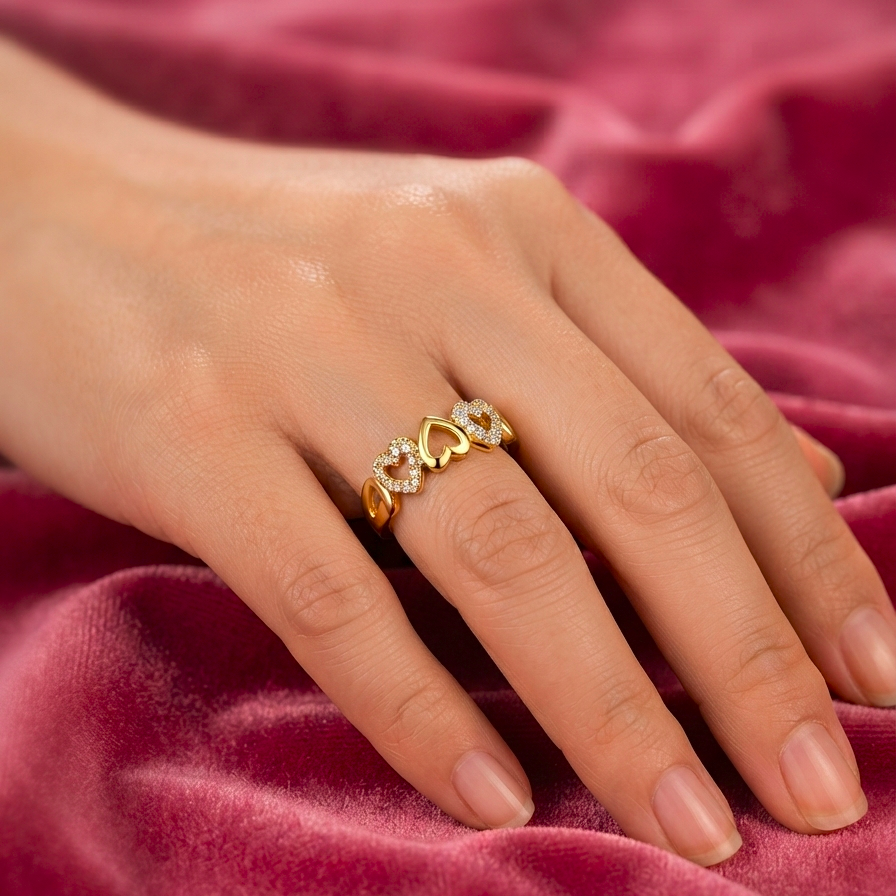 A close-up of a hand wearing a gold ring with small clear stones, resting on a draped dusty rose velvet fabric.