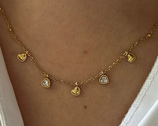 Gold necklace with heart-shaped pendants on a person wearing a white top.