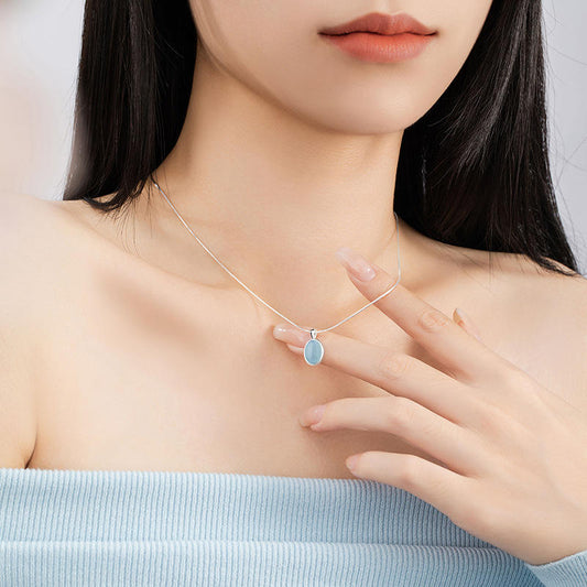 Woman wearing a necklace with a blue pendant, touching her chest.
