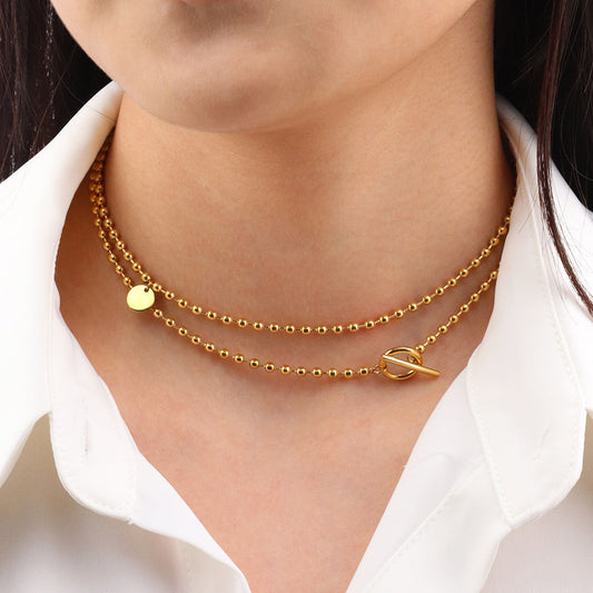 Gold necklace with a leaf pendant worn by a person against a white shirt background