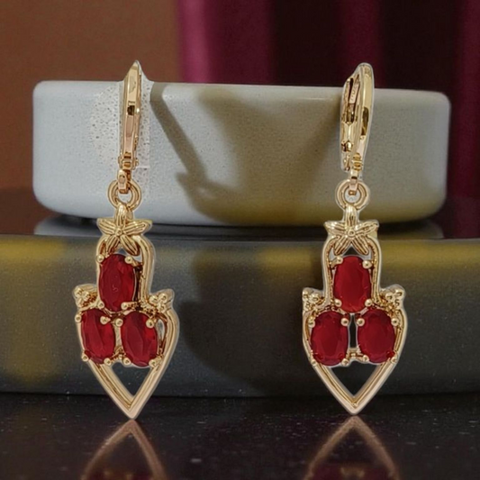 Gold earrings with red gemstones on a reflective surface