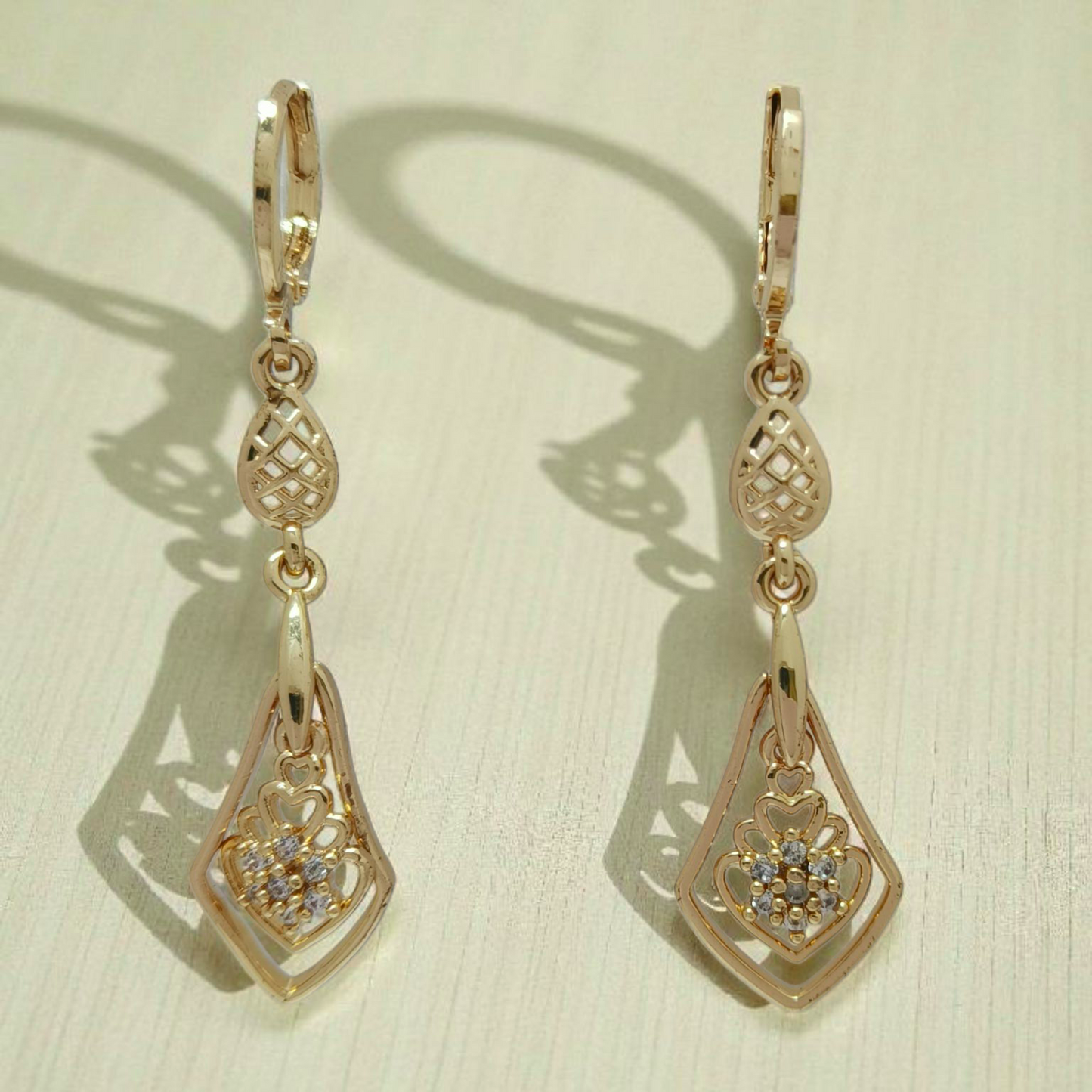 Pair of gold earrings with intricate designs on a beige background