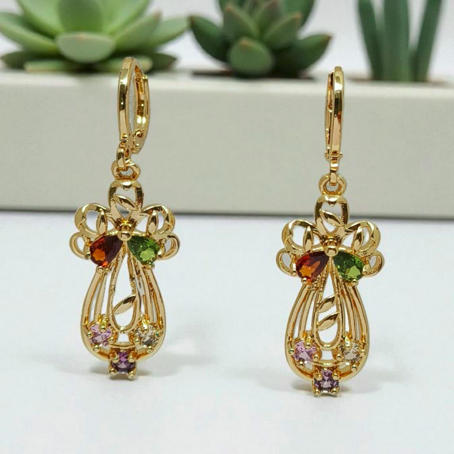 Gold earrings with gemstones on a white surface with succulents in the background