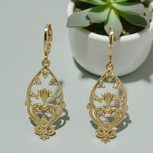 Gold earrings with intricate designs on a light gray background with a potted plant.