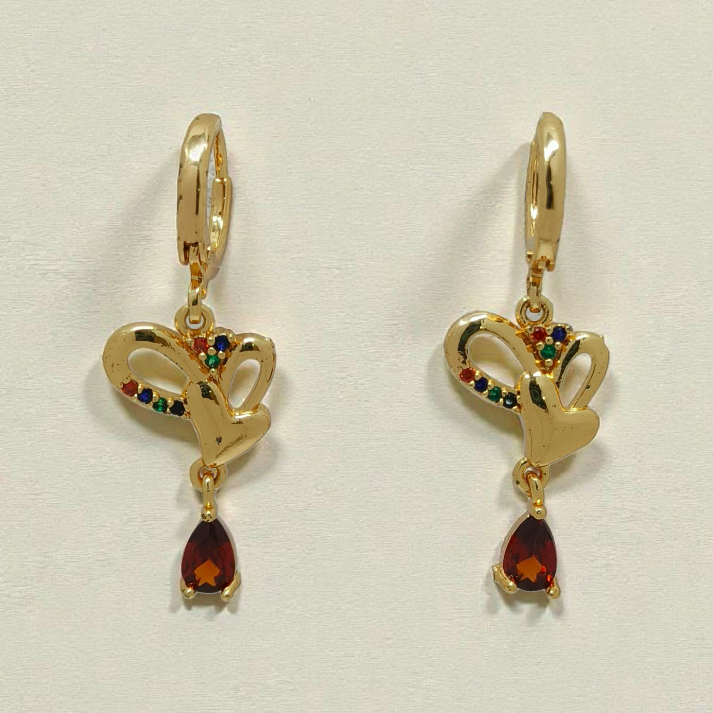 Gold earrings with heart designs and red gemstones on a light gray background