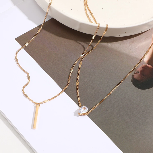 Two gold necklaces with pendants on a neutral background