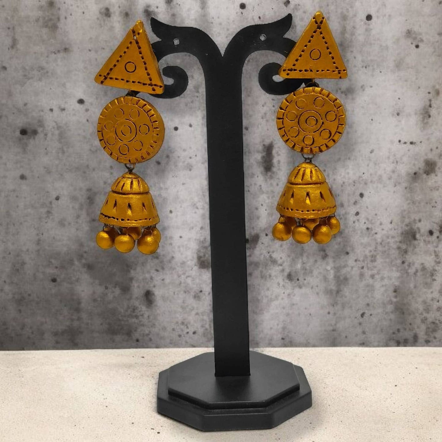 Handmade Terracotta Jhumka Earrings in yellow with intricate patterns displayed on black stand