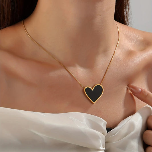 Heart-shaped necklace with black heart pendant on a person wearing a white top.