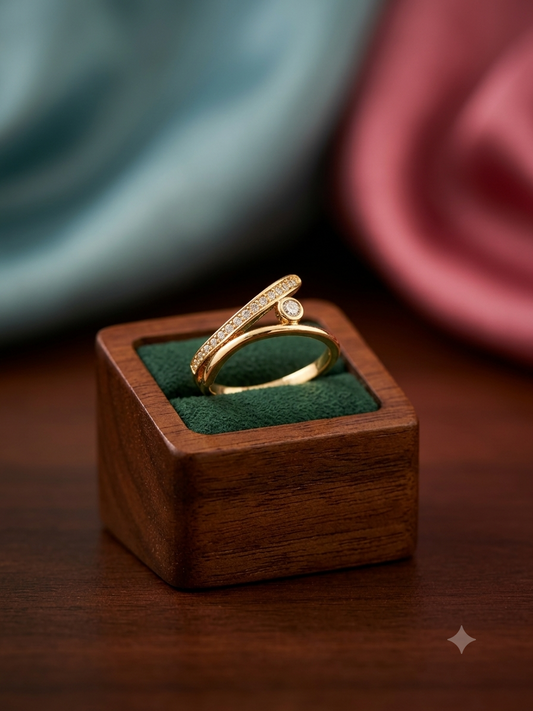 A gold ring with a pavé-set round diamond and a small center stone, displayed on a dark green velvet-lined wooden ring box on a wooden table.