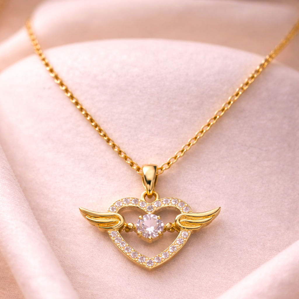 Gold necklace with a heart-shaped pendant featuring wings on a soft pink background