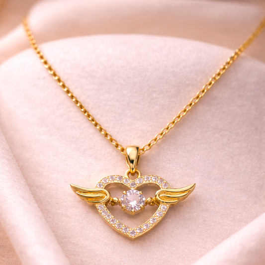 Gold necklace with a heart-shaped pendant featuring wings on a soft pink background