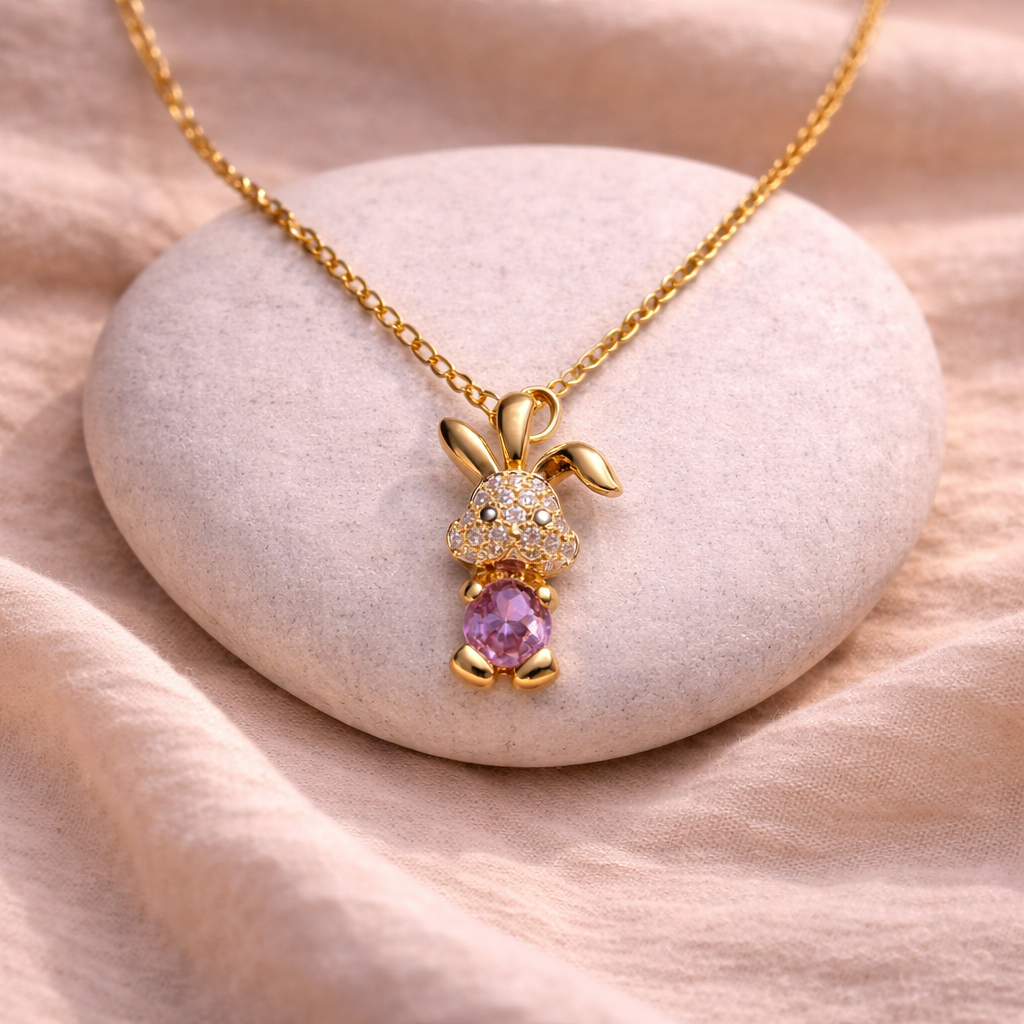 Gold bunny-shaped necklace with a pink gemstone on a stone surface