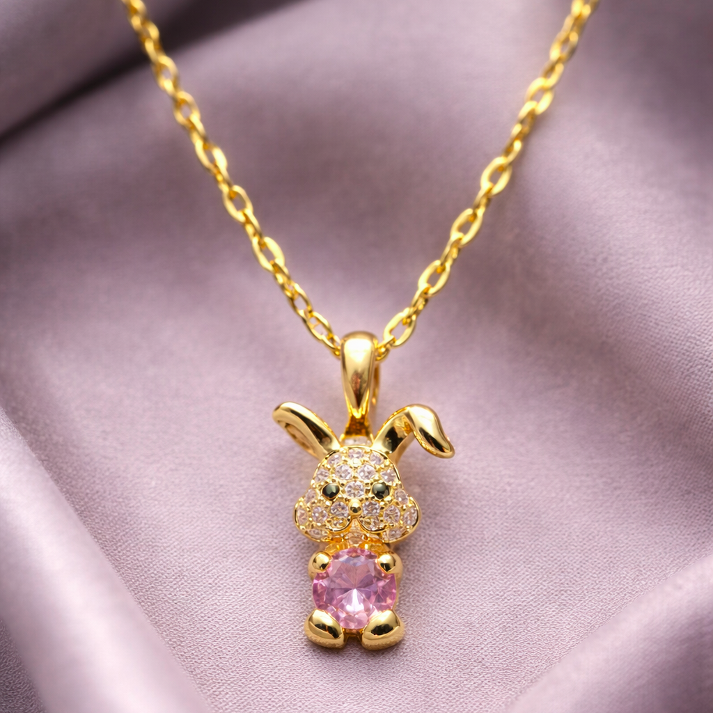 Gold bunny pendant necklace with pink heart on a soft fabric background