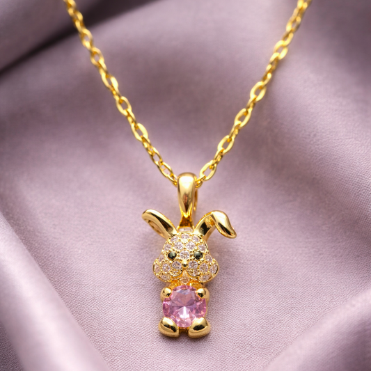 Gold bunny pendant necklace with pink heart on a soft fabric background
