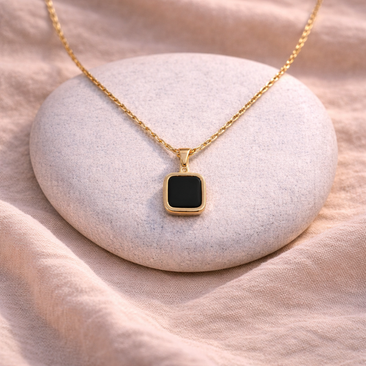 Gold necklace with a black square pendant on a white stone
