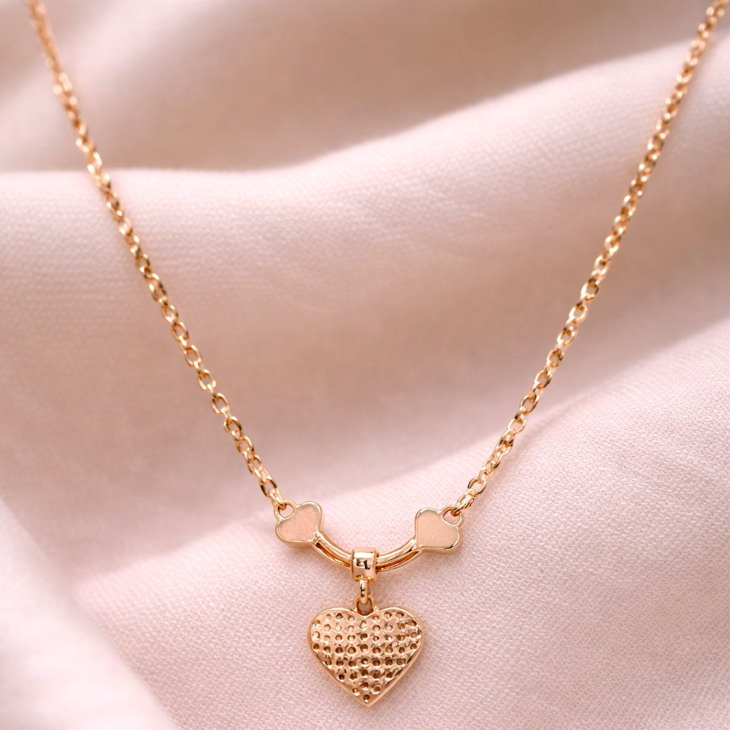 Gold necklace with a heart pendant on a soft pink fabric background