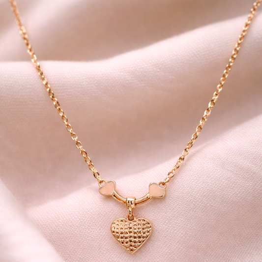Gold necklace with a heart pendant on a soft pink fabric background