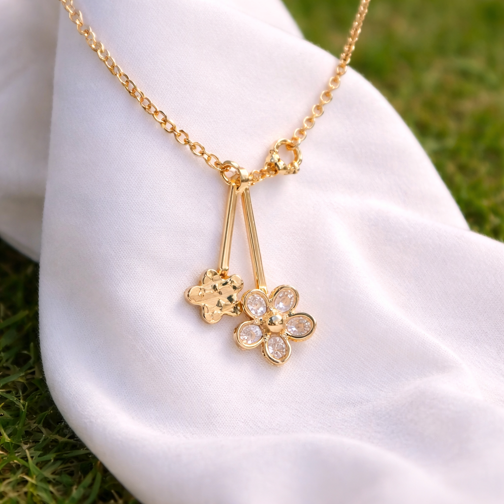 Gold necklace with flower pendants on a white hand against a grassy background