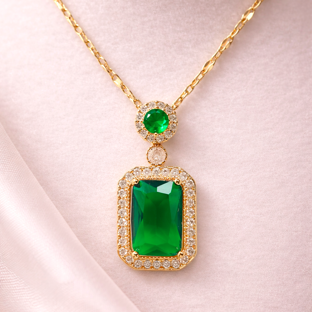 Gold necklace with green gemstone pendant on a light pink fabric background