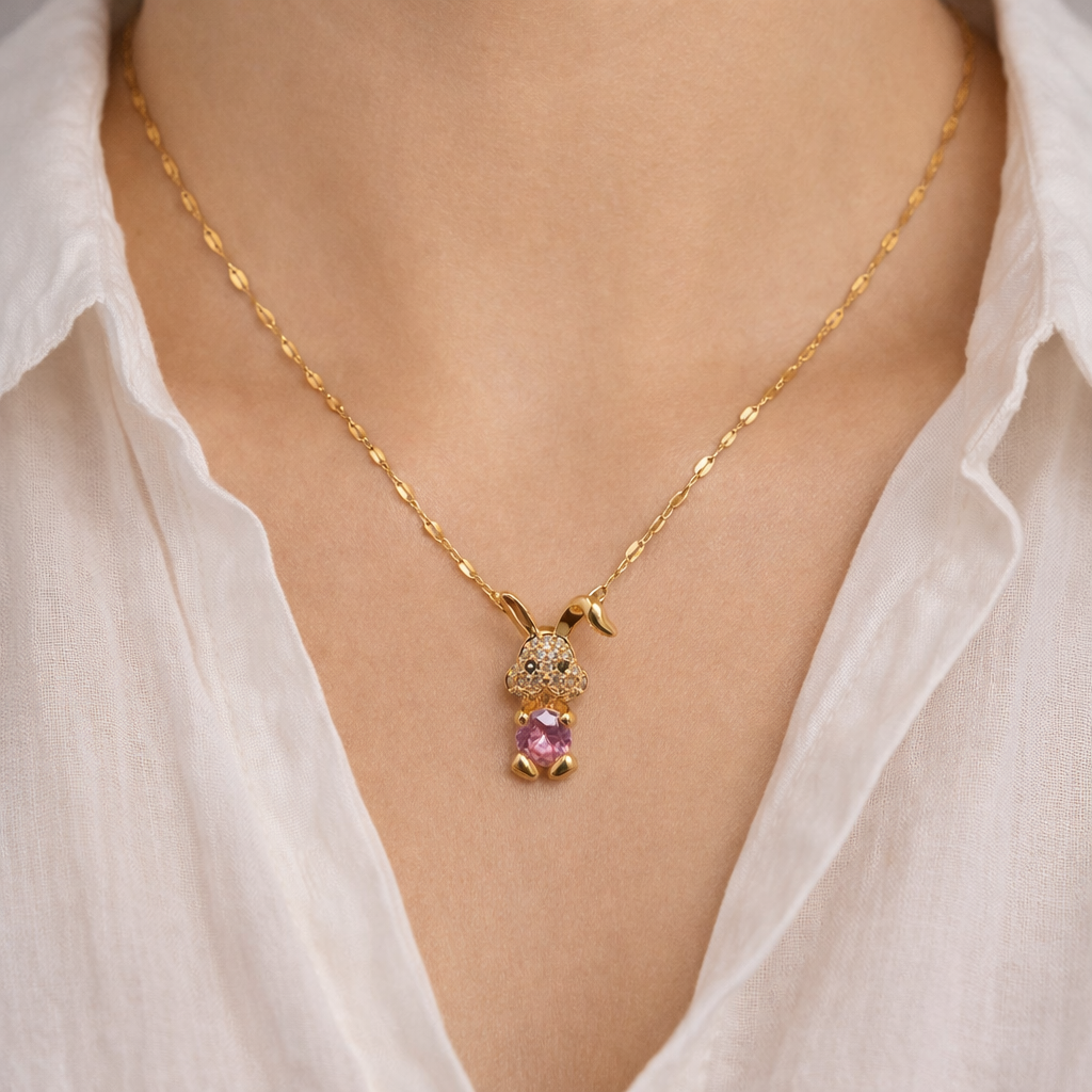 Gold necklace with a pink gemstone pendant on a white shirt background