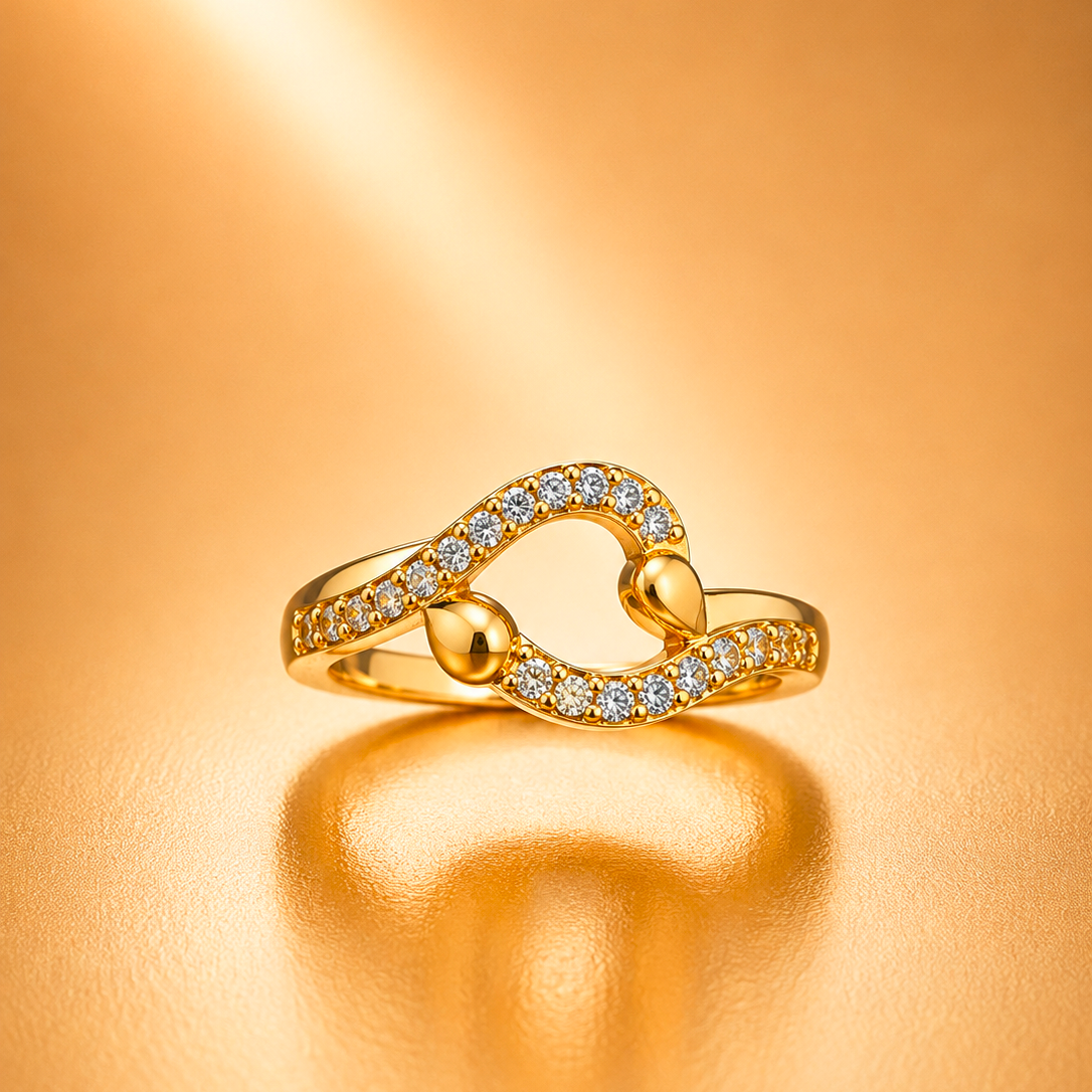 A gold ring with a heart-shaped design paved with small clear stones, resting on a warm, reflective gold surface.