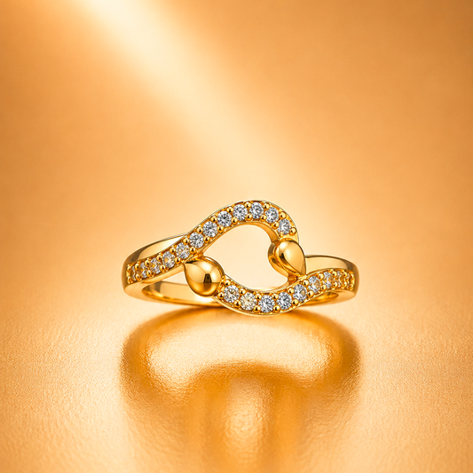 A gold ring with a heart-shaped design paved with small clear stones, resting on a warm, reflective gold surface.