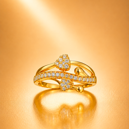 A gold ring with a heart-shaped cluster of small clear stones and a curved pavé band, photographed on a warm gold reflective surface.