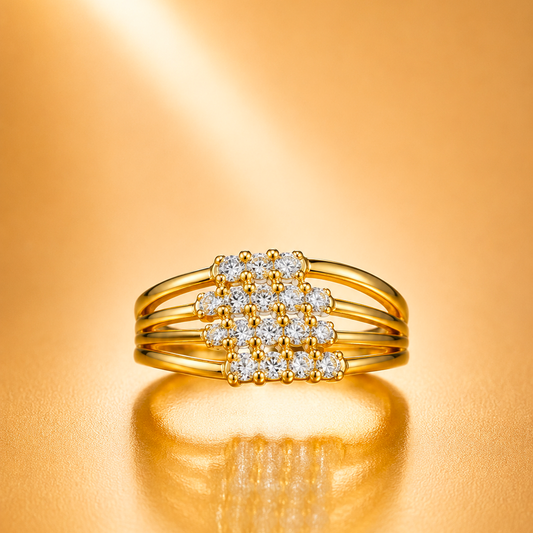 A gold ring with a square cluster of clear gemstones in the center, photographed on a warm gold reflective surface.