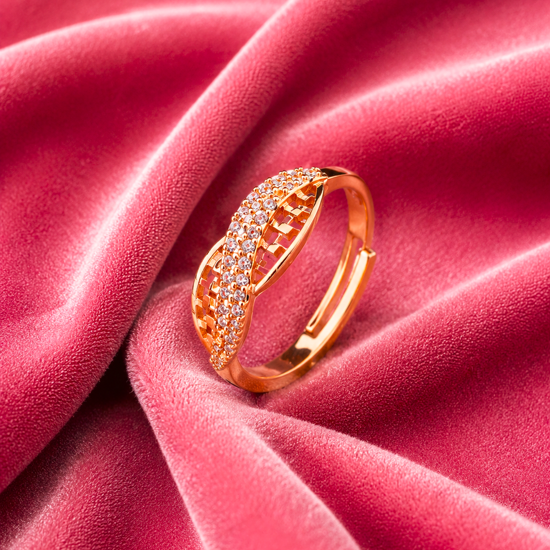 A rose gold ring with pavé-set clear stones, resting on draped dusty pink velvet fabric.
