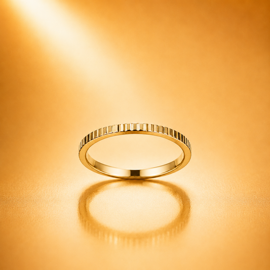 A slim gold eternity ring with a beaded, textured band sits on a warm, golden reflective surface with a soft reflection below.