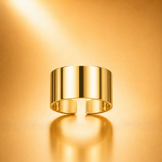A polished gold open cuff ring with a wide cylindrical band, shown on a warm gold reflective surface with a soft reflection.