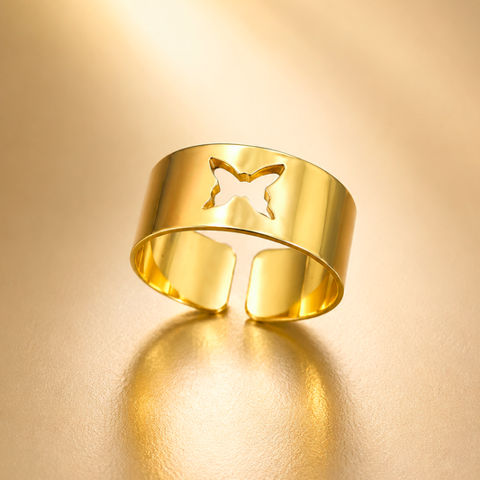 A polished gold open cuff ring with a butterfly-shaped cutout on the front, displayed on a warm, reflective gold surface.