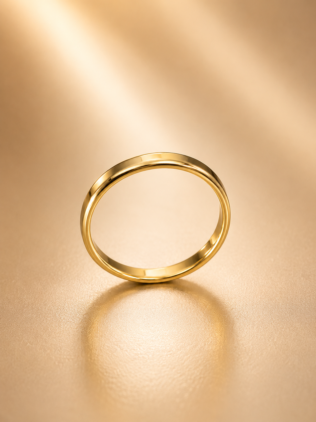 A minimalist gold band ring standing upright on a warm, textured gold surface with a soft reflection underneath.