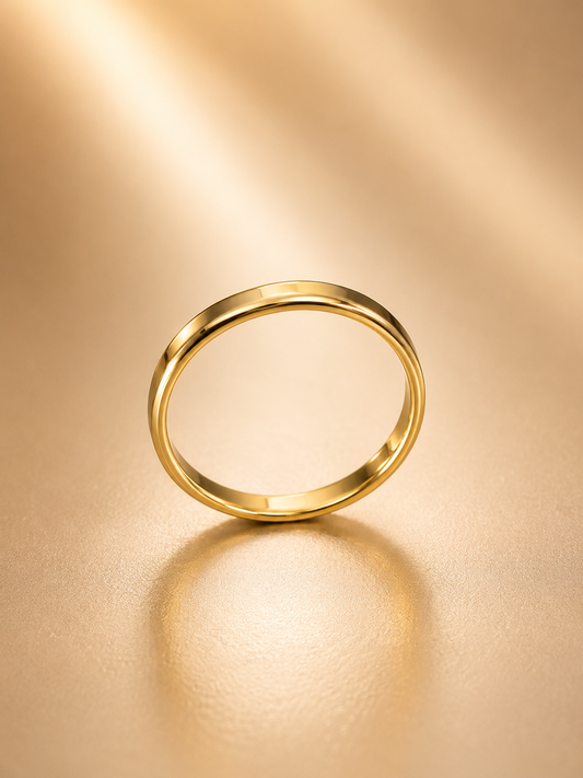 A minimalist gold band ring standing upright on a warm, textured gold surface with a soft reflection underneath.