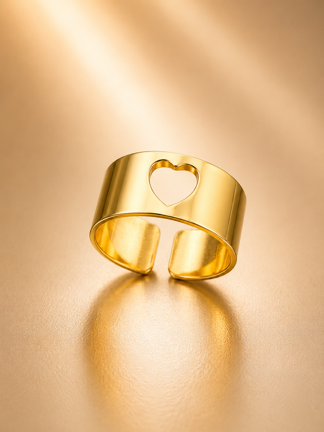 A polished gold open cuff ring with a heart-shaped cutout, displayed on a warm, reflective gold surface.