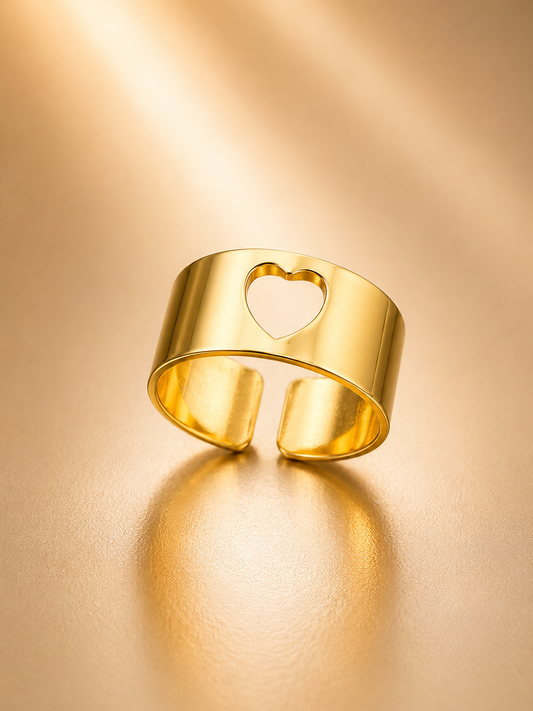A polished gold open cuff ring with a heart-shaped cutout, displayed on a warm, reflective gold surface.