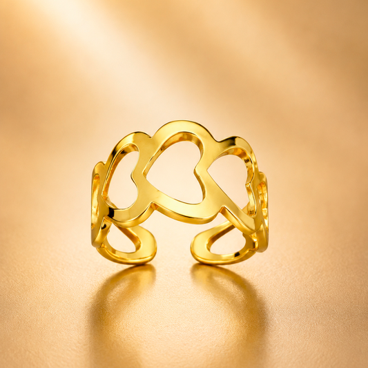 A gold openwork ring with a stylized, organic wavy shape, displayed on a warm, reflective gold surface.