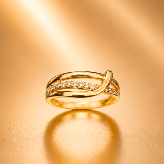 A gold ring with a double-band design, featuring one band paved with small clear stones, displayed on a warm, reflective gold surface.