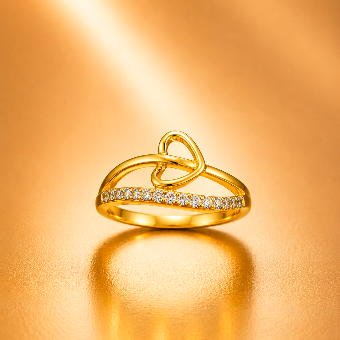 A gold ring with a double-loop knot design and a row of small clear stones along the front, photographed on a warm metallic gold background with a soft reflection below.