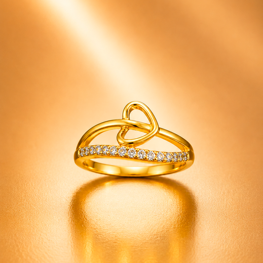 A gold ring with a double-loop knot design and a row of small clear stones along the front, photographed on a warm metallic gold background with a soft reflection below.