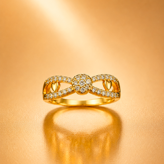 A gold ring with a bow-like openwork design, set with small clear stones, displayed on a warm gold reflective surface.