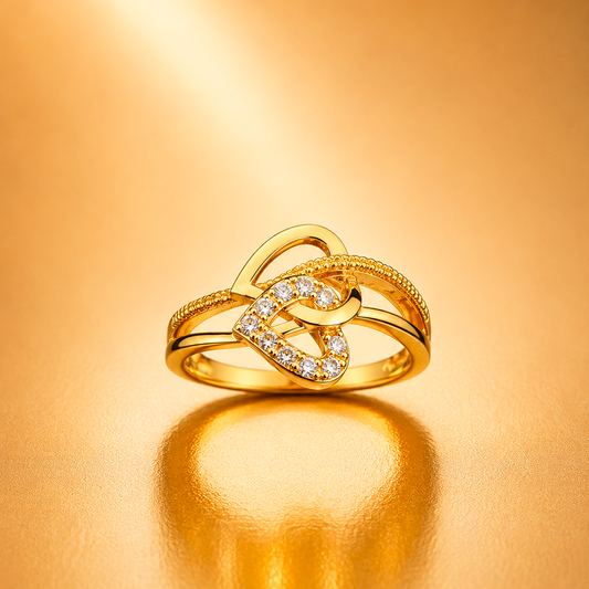 A gold ring with an intertwined knot design, featuring a pavé-set diamond heart in the center and textured beaded bands, displayed on a warm gold reflective surface.