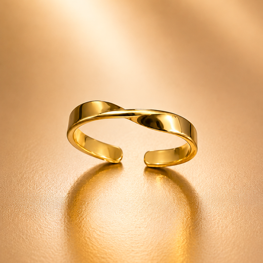 A polished gold open ring with a twisted, intertwined band design, resting on a warm, textured gold surface with a soft reflection.